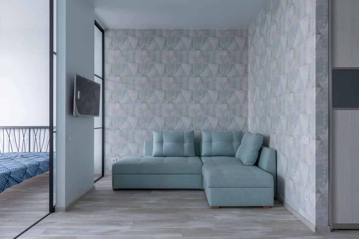 Un salon moderne avec canapé bleu, mur géométrique, parquet clair et fenêtre
